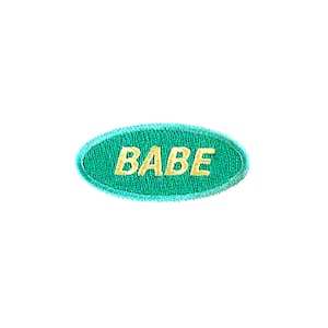 May include: A turquoise oval-shaped patch with the word "BABE" embroidered in yellow thread.