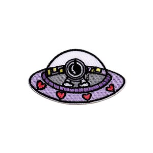 May include: Embroidered patch featuring a purple UFO with a white top and a smiling astronaut inside. The UFO has a heart design around the edge. The astronaut is wearing a white spacesuit with a black visor.