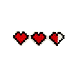 May include: A pixelated design featuring three red hearts with black outlines, reminiscent of a video game health bar. The heart on the right is partially white, indicating a reduced health level. The design is set against a plain white background.