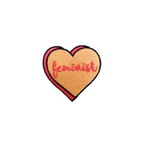 May include: A pink heart-shaped patch with the word "feminist" embroidered in red.