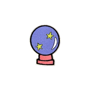 Puede incluir: Parche bordado con una bola de cristal azul con dos estrellas amarillas y una luna creciente blanca. La bola de cristal se asienta sobre una base roja con un contorno negro, ideal para añadir un toque mágico.