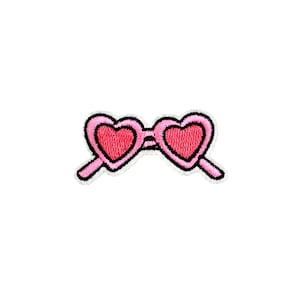 Puede incluir: Parche bordado de gafas de sol rosas en forma de corazón con contorno negro y borde blanco. Las lentes son de un tono rosa más oscuro. El parche está sobre un fondo blanco.