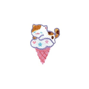Könnte beinhalten: Ein gestickter Bügelaufkleber mit einem Cartoon-Katzenmotiv, das auf einem rosa und weißen Eiswaffel mit einer wolkenförmigen Eiskugel sitzt. Die Katze hat braunes, weißes und orangefarbenes Fell und trägt ein violettes Halsband.