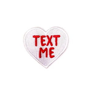 May include: White heart-shaped patch with red embroidered text that says "TEXT ME".