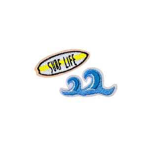 May include: Two embroidered iron-on patches, one with a surfboard and the text "Surf Life" in black, and the other with a blue wave.