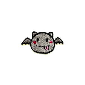 May include: A gray embroidered patch of a cartoon bat with a smiling face and a pink tongue sticking out. The bat has black wings and pink cheeks.