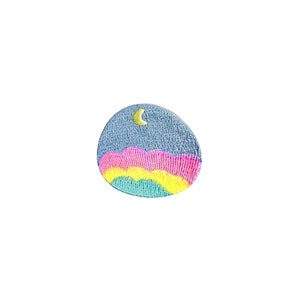May include: A round, blue embroidered patch with a yellow crescent moon and a rainbow-colored mountain range.