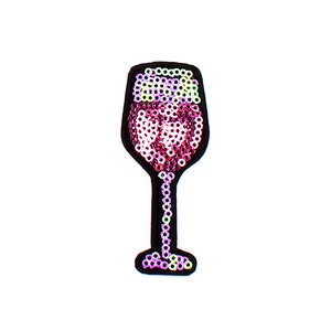 Może przedstawiać: Naszywka w kształcie kieliszka do wina z różowych i fioletowych cekinów. Kieliszek jest obwiedziony czarną ramką.