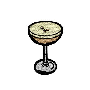 Puede incluir: Un parche bordado que representa una copa de martini con tres granos de café en la parte superior, en marrón y blanco.