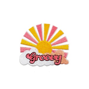 Könnte beinhalten: Gestickter Aufnäher mit einer gelben Sonne mit rosa und gelben Strahlen, über einer weißen Wolke mit dem Wort "Groovy" in rosa Schrift. Das Design hat einen Retro-Vintage-Stil.