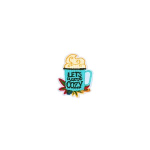 Pode incluir: Um remendo bordado para passar a ferro com uma caneca azul com borda branca e um redemoinho amarelo no topo. A caneca diz "Let's Get Cozy" em texto preto. A caneca é cercada por flores bordadas coloridas.