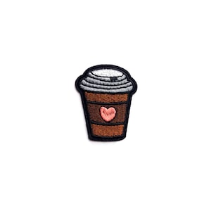 Può includere: Toppa ricamata da stirare a forma di tazza di caffè marrone con un cuore rosa sul lato. La tazza ha un coperchio bianco con un bordo grigio.