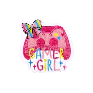 Könnte beinhalten: Gestickter Aufnäher mit einem rosa Videospiel-Controller-Design und den Worten "GAMER GIRL" in Gelb und Blau. Oben befindet sich eine bunte Schleife. Der Aufnäher hat einen weißen, genähten Rand.