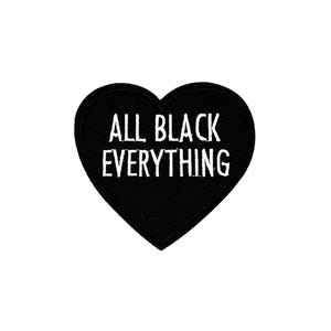 May include: A black heart-shaped patch with white embroidered text that reads "ALL BLACK EVERYTHING". The patch is set against a white background. This patch is suitable for jackets, bags, or other fabric items.