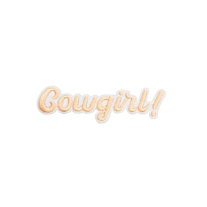 May include: A white embroidered patch with the text "Cowgirl!" in orange thread.