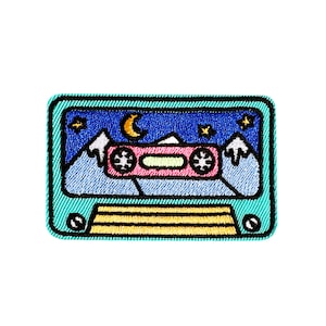 May include: A turquoise blue embroidered patch shaped like a cassette tape with a night sky scene inside. The scene includes mountains, stars, a crescent moon, and a pink cassette player.