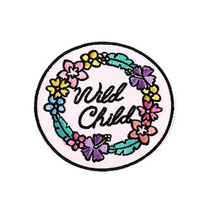 Könnte beinhalten: Gestickter Aufnäher mit weißem Hintergrund und schwarzem Rand. Der Aufnäher zeigt einen Blumenkranz in Rosa-, Gelb-, Lila- und Türkistönen, der die Worte "Wild Child" in schwarzer Schrift umgibt.