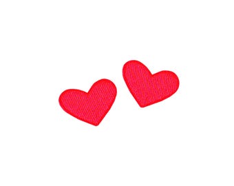 May include: Two red felt hearts on a white background.
