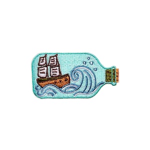 Peut inclure: Un patch brodé représentant une bouteille en verre bleu avec un bouchon en liège. À l'intérieur de la bouteille, un petit voilier brun avec des voiles blanches, naviguant sur des vagues bleues.