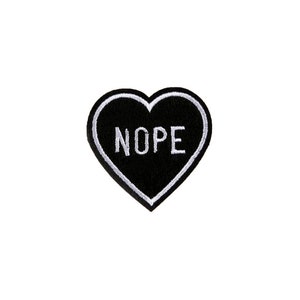 Puede incluir: Parche negro en forma de corazón con costuras blancas y la palabra "NOPE" en letras blancas.