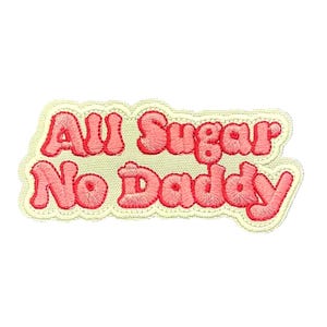 Pode incluir: Um remendo bordado rosa e branco com o texto "All Sugar No Daddy" em uma fonte retrô.