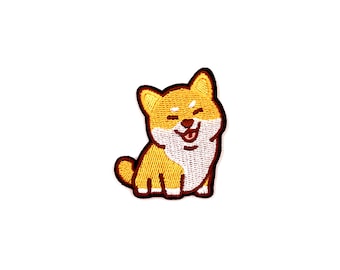 Puede incluir: Parche bordado de un perro Shiba Inu sonriente con contornos marrones y pecho blanco. El perro está sentado con la lengua fuera.