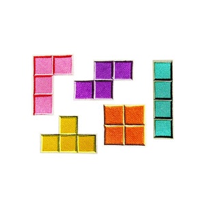 以下が含まれることがあります： カラフルな刺繍のテトリスブロック6個セット。ブロックの色はピンク、パープル、イエロー、オレンジ、ターコイズです。