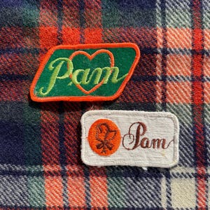 May include: Two vintage patches on a plaid background. One patch is green with the name "Pam" in cursive and a heart, outlined in orange. The other patch is rectangular, with the name "Pam" and a floral design.
