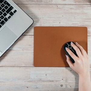 May include: A brown leather mouse pad with a black wireless mouse on top. The mouse has a gold ring around the scroll wheel.