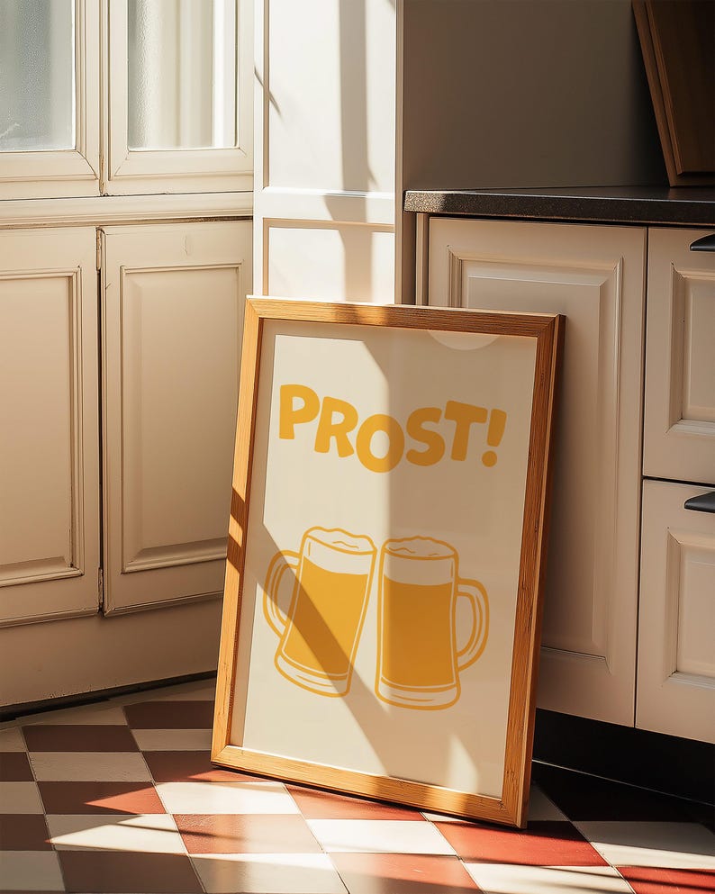 May include: A framed print with a light yellow background and a wooden frame. The print features two yellow beer mugs with the word "PROST!" in yellow letters.