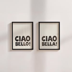 Op de afbeelding: Twee ingelijste kunstdrukken met zwarte lijsten en gebroken witte achtergronden. Elke print bevat de woorden "CIAO BELLO!" en "CIAO BELLA!" in vette, zwarte letters. De prints worden tegen een witte muur getoond.