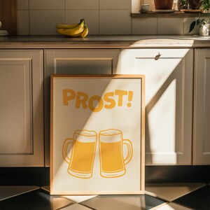 May include: A framed print with the word "PROST!" in yellow letters and two yellow beer mugs with foam on top.