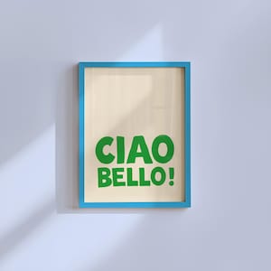 May include: A framed art print with a light beige background and the words "CIAO BELLO!" in bold green letters. The frame is a bright blue, and the artwork is displayed against a white wall.