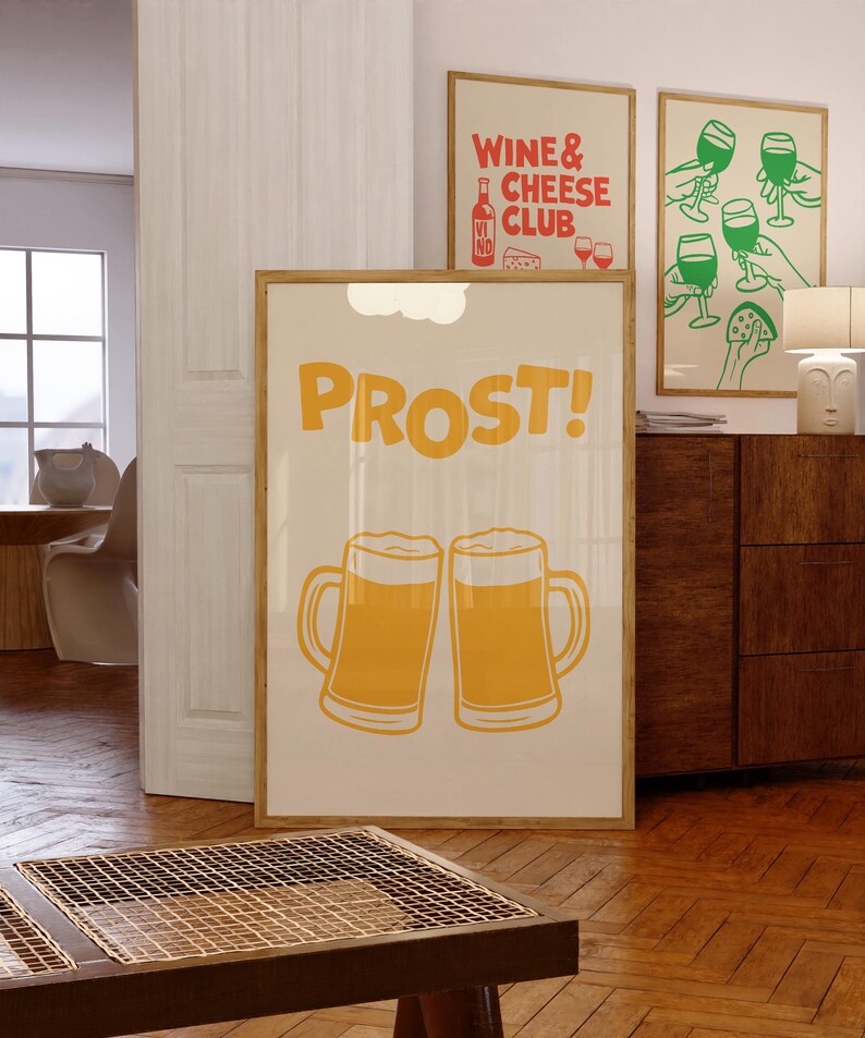 A beige poster with the word "PROST!" in yellow letters and two yellow beer mugs clinking together. The poster is framed in wood and hanging on a wall.