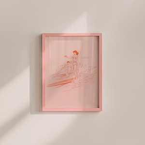 May include: A framed art print featuring a line drawing of two people surfing. The artwork is in shades of orange and pink, with a pink frame. The image depicts a woman and a child on surfboards in the ocean.