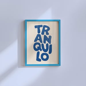 May include: A framed art print with the word "TRANQUILO" in bold, blue letters. The artwork is set against a cream-colored background and framed in a bright blue frame. The print is displayed on a white wall.