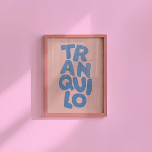 May include: A framed art print with the word "TRANQUILO" in blue bubble letters. The frame is a light pink colour, and the background is a soft pink. The artwork is displayed on a pink wall.