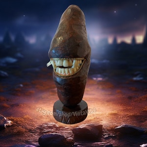 May include: A dark brown, rock-like sculpture with a zipper mouth revealing a set of white teeth. The sculpture is standing on a dark brown base against a dark blue background with stars.