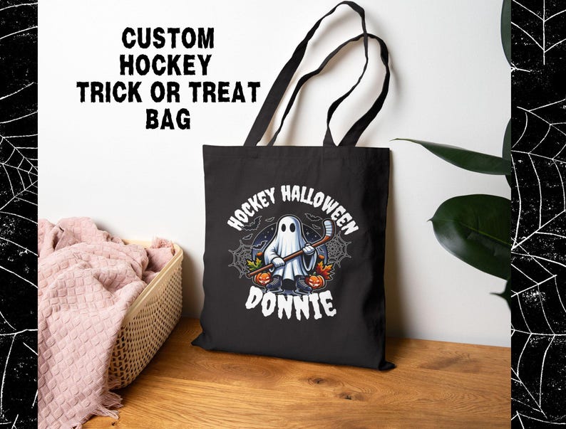 K&ouml;nnte beinhalten: Eine schwarze Tragetasche mit einer Grafik eines Geistes, der Schlittschuhe tr&auml;gt und einen Hockeyschl&auml;ger h&auml;lt, umgeben von K&uuml;rbissen und Spinnenweben. Der Text lautet HOCKEY HALLOWEEN DONNIE. Die Tasche hat zwei schwarze Schulterriemen.