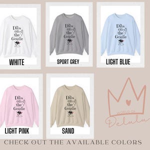 May include: A graphic sweatshirt with the text "Dibs on the Goalie" and a cartoon goalie. The sweatshirt is available in white, sport grey, light blue, light pink, and sand.
