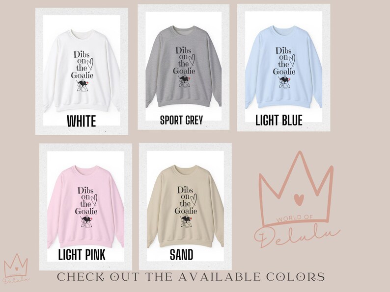 May include: A graphic sweatshirt with the text "Dibs on the Goalie" and a cartoon goalie. The sweatshirt is available in white, sport grey, light blue, light pink, and sand.