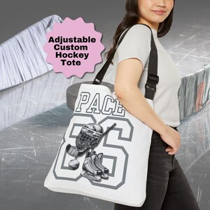 May include: White canvas tote bag with adjustable straps. The bag features a hockey design with a player's name "PACE" and number "86" in gray. A hockey helmet, stick, and skates are also included in the design.