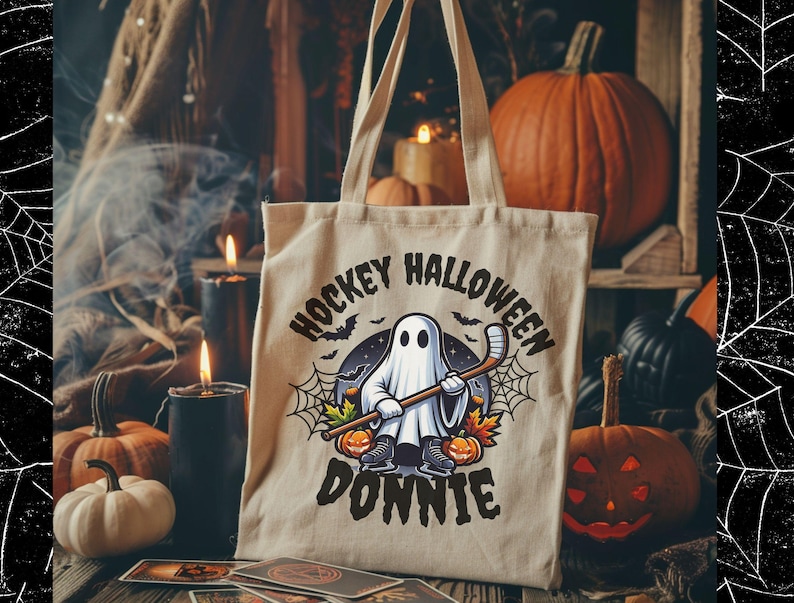K&ouml;nnte beinhalten: Eine beige Tragetasche aus Segeltuch mit einer Grafik eines Geistes, der Schlittschuhe tr&auml;gt und einen Hockeyschl&auml;ger h&auml;lt. Der Text HOCKEY HALLOWEEN DONNIE ist von Spinnweben, Flederm&auml;usen und K&uuml;rbissen umgeben, gedruckt in Schwarz und Orange.