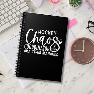 Puede incluir: Cuaderno negro de espiral con texto blanco que dice "HOCKEY Chaos COORDINATOR AKA TEAM MANAGER". El texto está en una fuente estilizada con un gráfico de palo de hockey y disco.