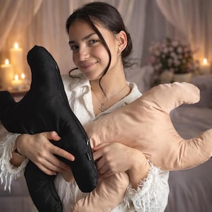 May include: Two plush pillows in the shape of hands. One pillow is black, and the other is a light tan color. The pillows are being held by a person wearing a white shirt.