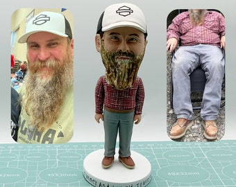 May include: A bobblehead figurine of a man with a beard wearing a red and black plaid shirt, blue jeans, and a white baseball cap with a black Harley Davidson logo. The figurine is standing on a white base with the words "Farmer Andy World Travel" written on it. The figurine is on a green cutting mat with white markings.