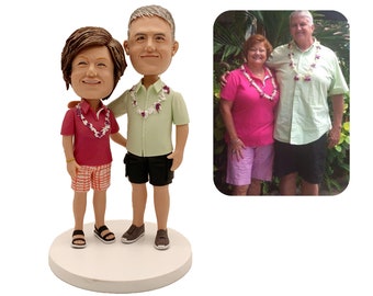 May include: A custom-made cake topper featuring a couple in a Hawaiian theme. The couple are wearing leis and tropical clothing. The topper is made of painted ceramic and is approximately 15 cm tall.