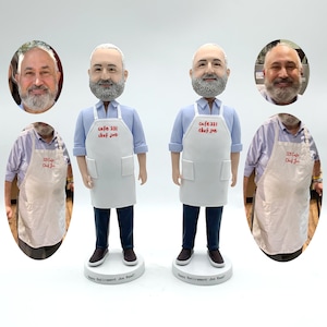 May include: Two custom-made figurines of a person wearing a blue shirt and a white apron with the text "Cafe 331 Chef Joe" on it. The figurines are standing on a base with the text "Happy Retirement Joe Rasl!"