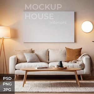 May include: A white sofa with brown and beige pillows in a living room with a large white framed canvas with the text "MOCKUP HOUSE Interiors" on the wall. There is a wooden coffee table in front of the sofa with a book and two vases on it. A wooden floor lamp with a white shade is in the corner of the room.
