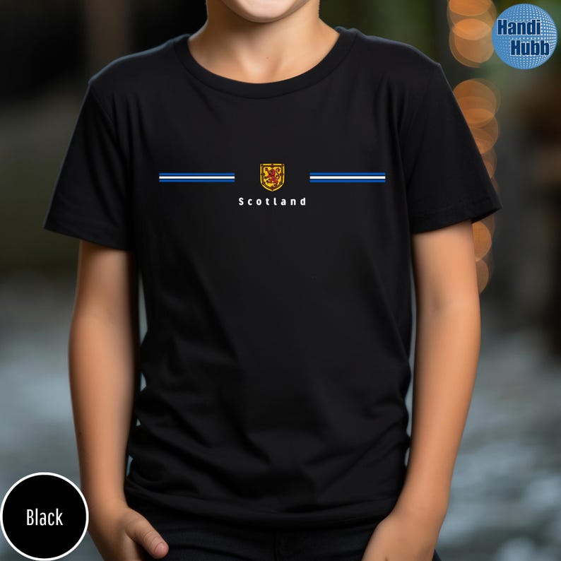 May include: Black t-shirt featuring the word "Scotland" in white, with a crest and blue and white stripes. The shirt has a crew neck and short sleeves. The shirt is made of a soft, comfortable material.